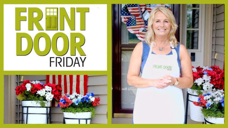 Front Door Friday – Smiling woman on a Patriotic porch with a wreath made of USA flag plates, and potted geraniums.