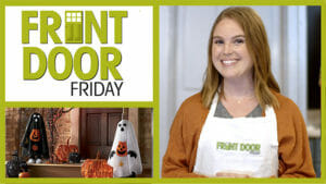 Front Door Friday – Smiling woman in an apron – A porch with two ghost figures and lit black and orange pumpkins.